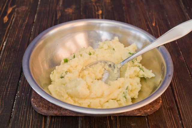 Разминаем отваренный картофель, добавляем сливочное масло и зелёный лук