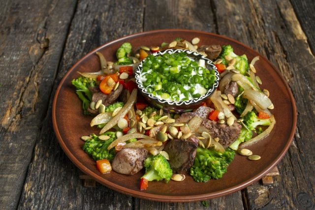 Посыпаем диетический салат из куриной печени с овощами семечками, подаём на стол с соусом