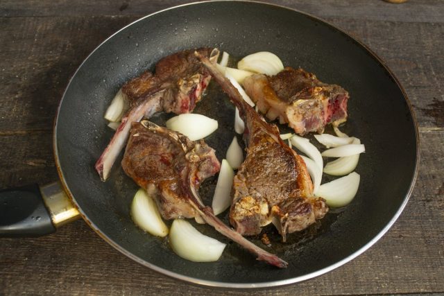 Кладём нарезанный лук на сковороду между кусками мяса Кладём нарезанный лук на сковороду между кусками мяса