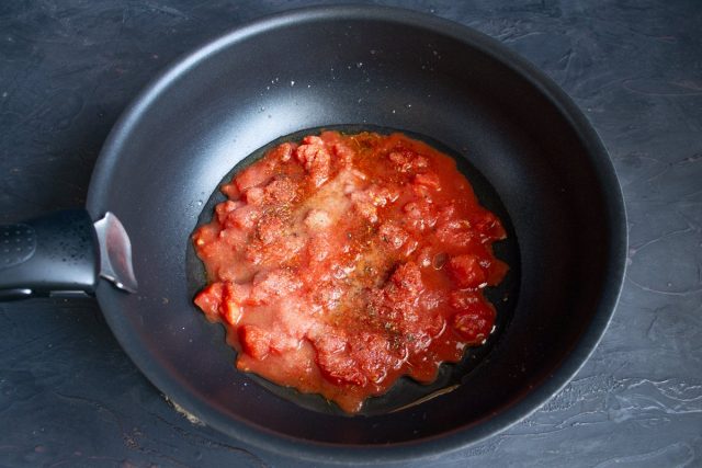 Наливаем в вок оливковое масло, выкладываем консервированные томаты вместе с соусом и приправляем 