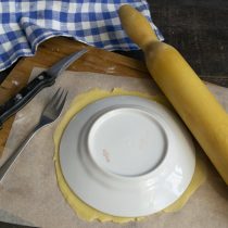 На листе пекарской бумаги раскатываем кусок теста тонко, прикладываем тарелку, вырезаем корж
