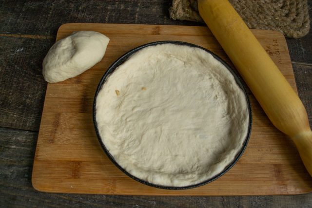 Кладём тесто в чугунную сковороду, растягиваем, формируем круглую основу с бортиком