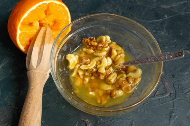 Смешиваем в миске обжаренные орехи, мёд, выжимаем сок апельсина