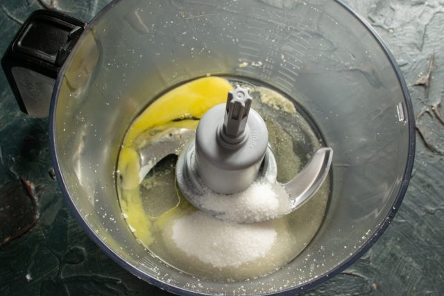 В чашу блендера насыпаем мелкий белый сахар, ванильный сахар. Разбиваем куриное яйцо, наливаем растительное масло
