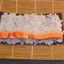 Выкладываем полоски лосося на рис, отступив от края ролла пару сантиметров
