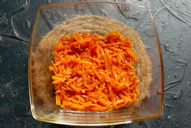 На дно прозрачной салатницы выкладываем тёртую морковь