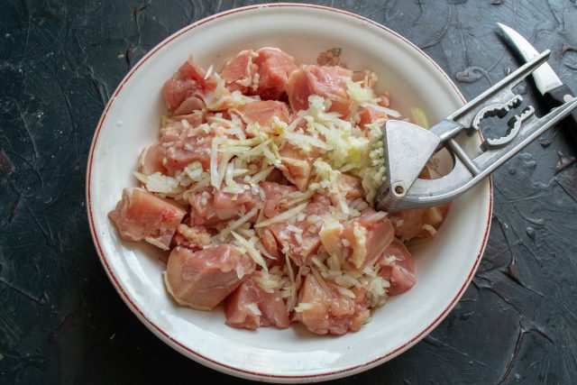 Мякоть куриного бедра нарезаем кусочками размером около двух сантиметров. Мелко режем репчатый лук, выдавливаем чеснок и ими посыпаем курицу Мякоть куриного бедра нарезаем кусочками размером около двух сантиметров. Мелко режем репчатый лук, выдавливаем чеснок и ими посыпаем курицу