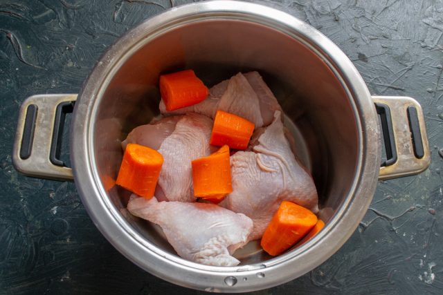 Четверти цыпленка промываем холодной водой, разрезаем по бедренному суставу и кладём на дно кастрюли. Кладём большую морковку, нарезанную крупно. Если есть пастернак или корень сельдерея, то этими овощами заменяют морковку