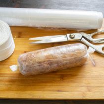 Выкладываем подготовленный фарш на пищевую пленку, заворачиваем колбаску