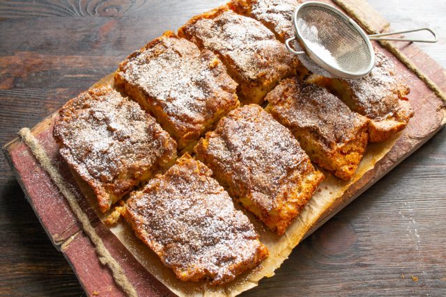 Остывший яблочный пирог с шампанским нарезаем на порции, посыпаем сахарной пудрой