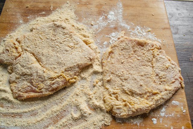 Насыпаем на разделочную доску молотые сухари. Кладем шницели в сухари.