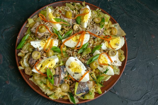 Посыпаем готовый рыбный салат с сайрой и оливками толченым черным перцем и зелёным луком и сразу подаём на стол.