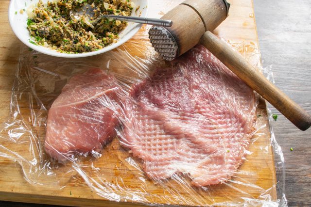 Берём два куска нежирной свинины толщиной около 1 см, накрываем их пищевой плёнкой и отбиваем молоточком с обеих сторон, стараясь сделать мясо максимально тонким и равномерным.