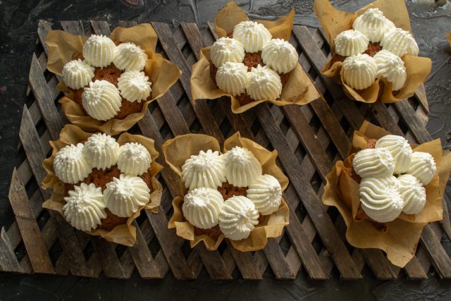 Для декора взбиваем холодные сливки с пудрой до устойчивых пиков. Перекладываем крем в кондитерский мешок с фигурной насадкой и украшаем полностью остывшие кексы.