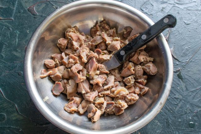 Остужаем вареные желудки и нарезаем их мелкими кусочками. Перекладываем измельченное мясо в глубокую миску — это основа нашего сытного салата.