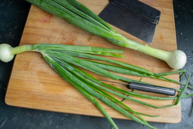 Разрезаем перья зеленого лука вдоль пополам и тщательно промываем их под струей холодной воды. Этот способ позволяет удалить скрытые загрязнения внутри.