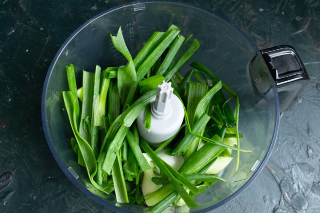Мелко шинкуем промытый зеленый лук вместе с белыми головками ножом. Перекладываем измельченную луковую массу в чашу блендера.