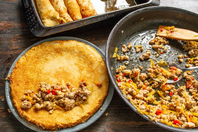 Смазываем форму маслом. Кладем ложку начинки на край блина, сворачиваем его плотной трубочкой и укладываем в подготовленную глубокую емкость швом вниз.