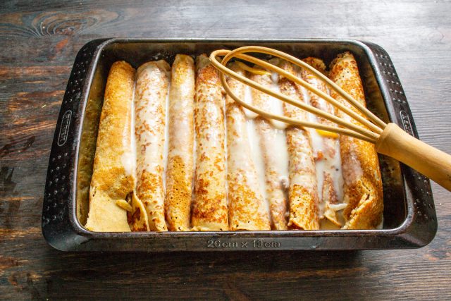 Равномерно заливаем уложенные в форму фаршированные блины горячим сметанным соусом. Следим, чтобы жидкость полностью покрыла поверхность всех изделий.