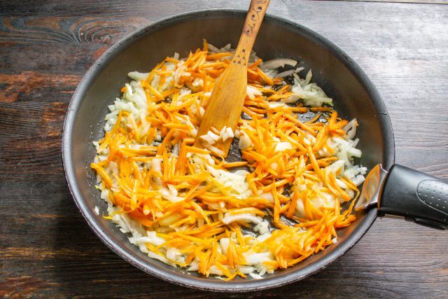 Натираем очищенную морковь на крупной терке. Добавляем к луку и пассеруем овощную смесь вместе еще пять минут, периодически помешивая деревянной лопаткой.
