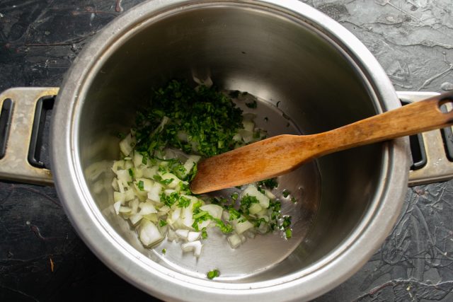 Измельчаем репчатый лук, чеснок и зелень петрушки. Обжариваем овощи в кастрюле с толстым дном на растительном масле до появления яркого аромата.