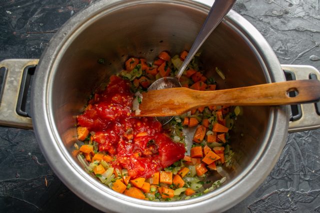 Нарезаем очищенную морковь кубиками и отправляем к луку. Через пять минут добавляем размятые консервированные томаты и тушим массу десять минут.