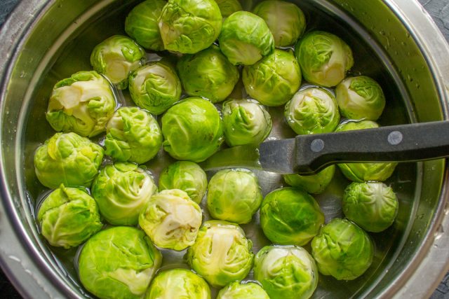 Срезаем жесткие кочерыжки у брюссельской капусты и аккуратно снимаем верхние листья. Промываем кочанчики водой, крупные экземпляры разрезаем пополам.