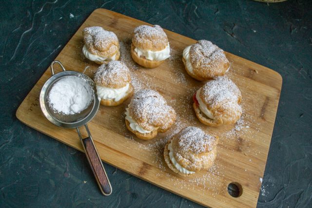Обильно посыпаем собранные профитроли сахарной пудрой через мелкое ситечко. Декорируем выпечку непосредственно перед подачей для эстетичного вида.