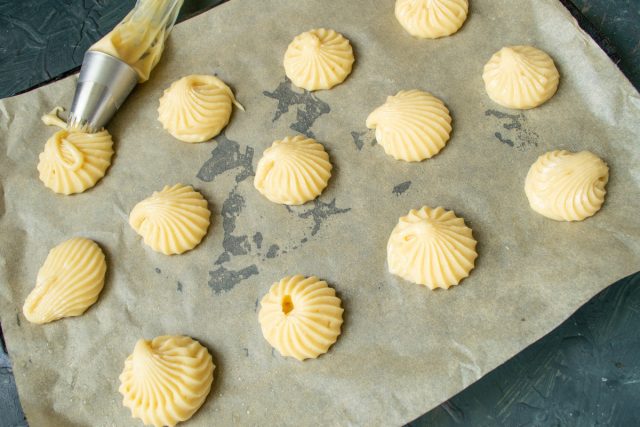 Перекладываем тесто в кондитерский мешок с насадкой. Отсаживаем небольшие шарики на пергамент, оставляя расстояние для увеличения объема при выпечке.