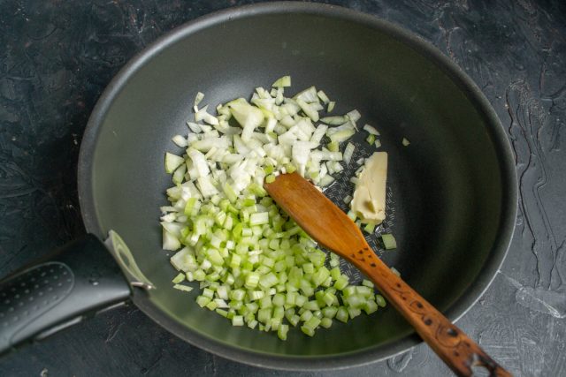 Высыпаем к луку измельченные стебли сельдерея. Пассеруем овощную смесь около десяти минут, периодически помешивая, пока кусочки не станут мягкими.
