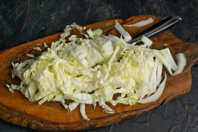 Удаляем жесткие уплотнения у основания листьев пекинской капусты. Шинкуем нежную зеленую часть полосками шириной один сантиметр для основы салата.