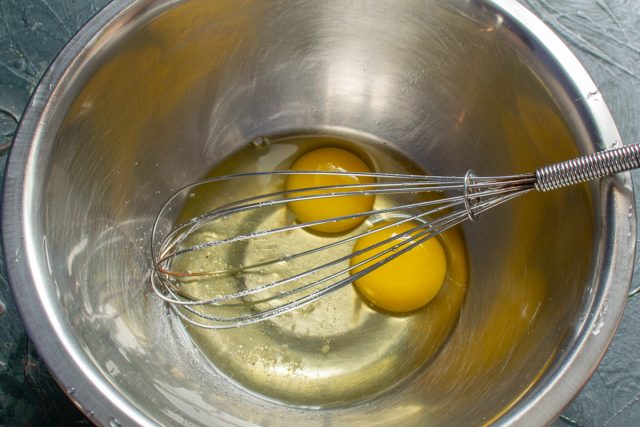 Разбиваем в глубокую миску сырые куриные яйца и добавляем соль. Взбиваем массу венчиком до получения полностью однородного яичного состояния.