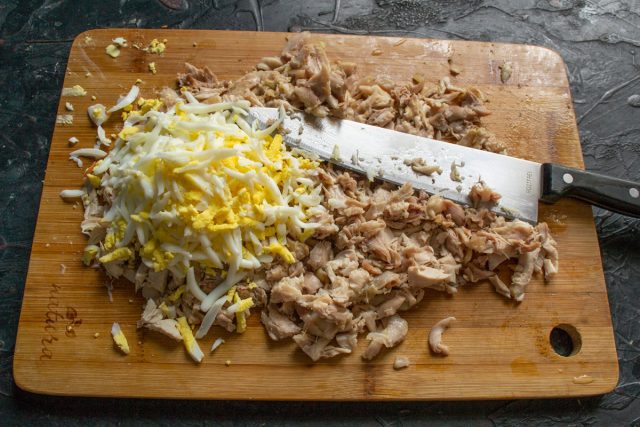 Очищаем сваренные вкрутую яйца и добавляем их к куриному филе. Измельчаем ножом мясо вместе с яйцами, чтобы получить однородную рассыпчатую массу.