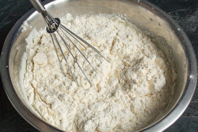 Всыпаем просеянную пшеничную муку в яично-молочную смесь. Интенсивно вымешиваем тесто венчиком, разбивая все комочки до гладкой консистенции.