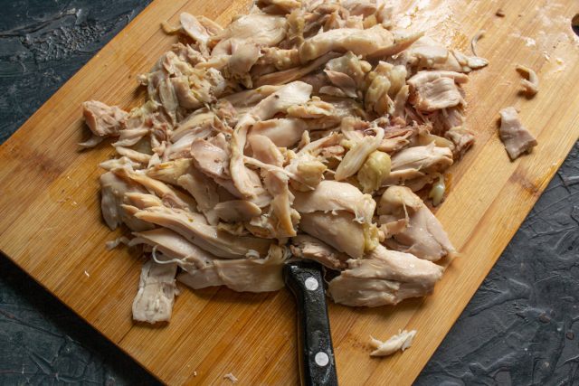 Достаем остывшую курицу из бульона, отделяем мясо от костей и удаляем кожу. Процеживаем бульон через сито, он понадобится нам для заливки.