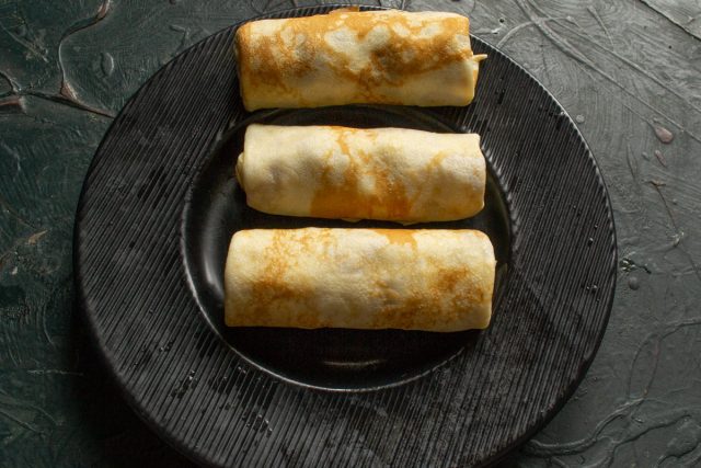 Сворачиваем фаршированные блины в плотные аккуратные трубочки. Из указанного объема ингредиентов формируем 8–10 штук в зависимости от размера сковороды.