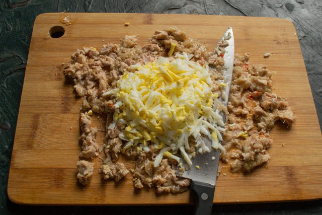 Измельчаем сваренные вкрутую яйца ножом или натираем их на крупной терке. Смешиваем яйца с тушенкой, добавляем соль и черный перец по вкусу.