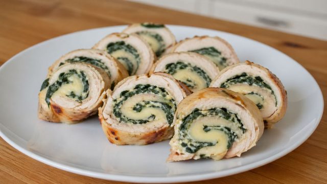 Куриное филе, свернутое с начинкой из шпината и сыра. При нарезке видна плотная спираль и сочная текстура внутри. Куриное филе, свернутое с начинкой из шпината и сыра. При нарезке видна плотная спираль и сочная текстура внутри.