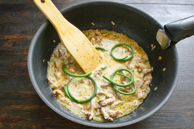 Кладем в сковороду скрученные кольцами верхушки чесночных стрелок, закрываем крышкой и томим мясо на слабом огне до мягкости в течение двадцати пяти или сорока минут.