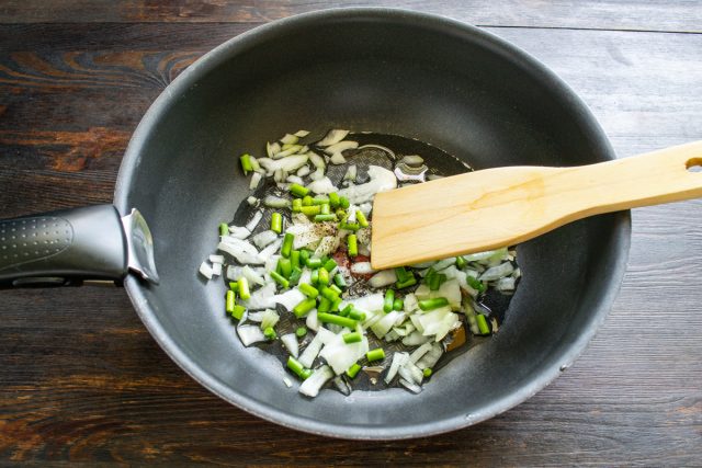 Нарезаем чесночные стрелки и репчатый лук небольшими кубиками, отправляем овощи в глубокую сковороду с маслом и обжариваем их на медленном огне до прозрачности лука.