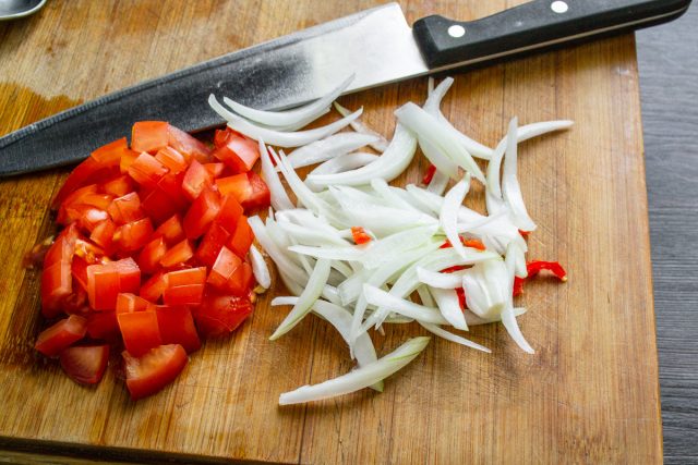 Нарезка репчатого лука перьями и спелых помидоров кубиками на доске